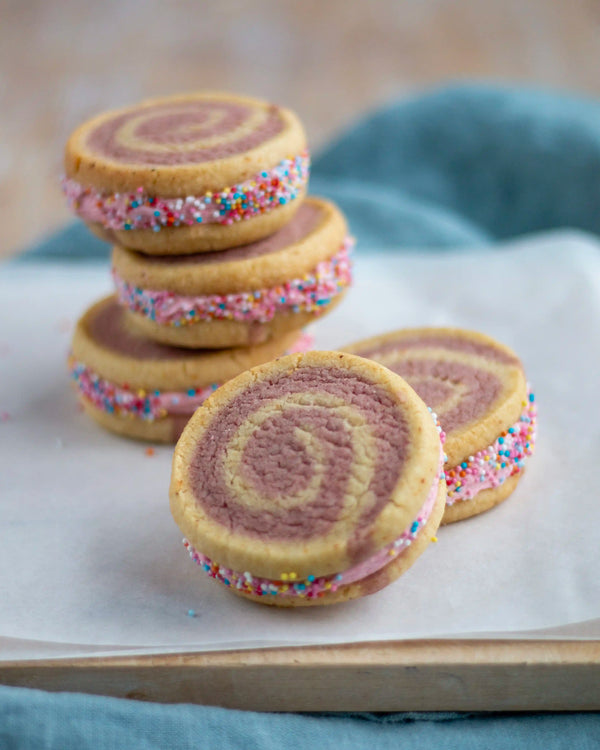 Honeywell Bakes Limited Edition Raspberry Swirl Sandwich Biscuits - rainbow swirled biscuits with a pink buttercream filling, rolled in sprinkled on greaseproof paper