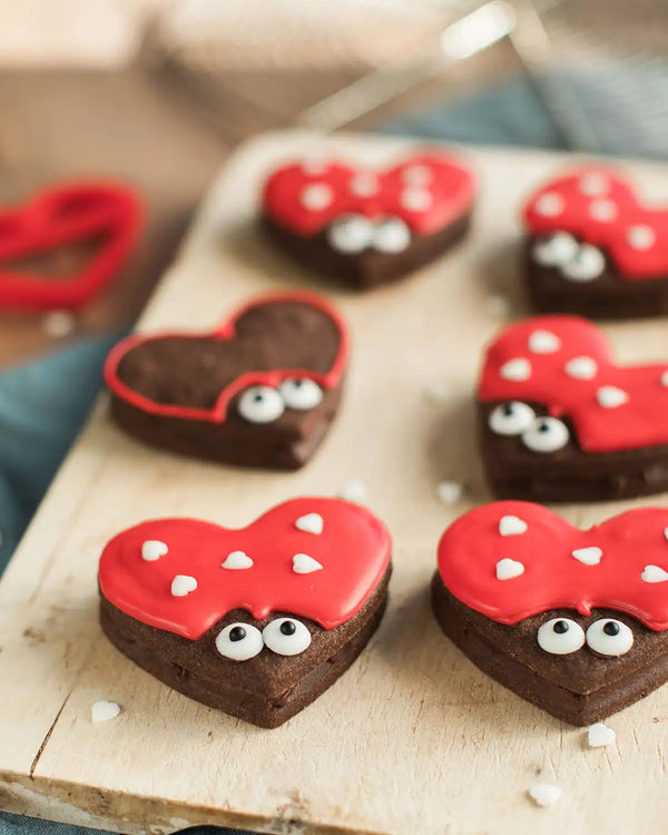 Honeywell Bakes Love Bug Biscuit Baking Kit - Heart-shaped cookies with red icing, white dots, and black eyes on a wooden board.