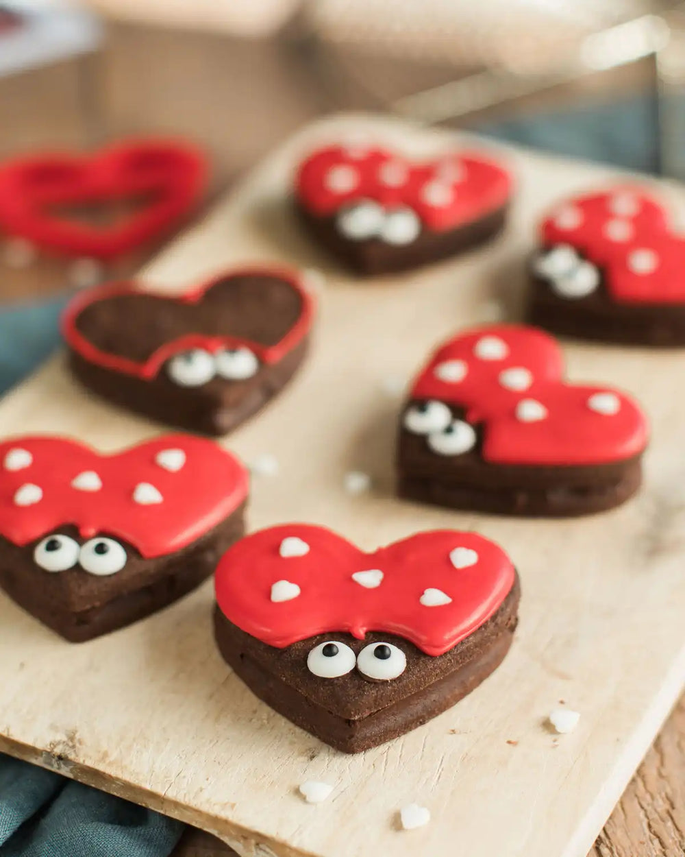 Honeywell Bakes Love Bug Biscuit Baking Kit - Heart-shaped cookies with red icing, chocolate bodies, and white candy eyes on a wooden surface.