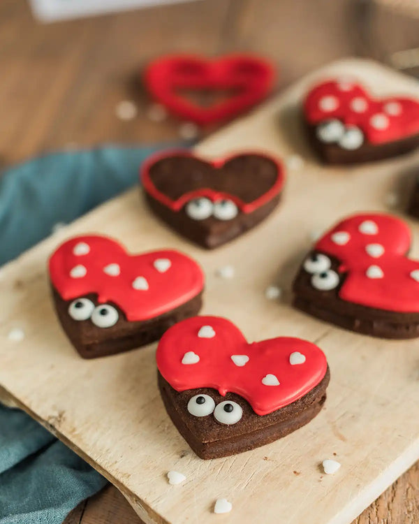 Honeywell Bakes Love Bug Biscuit Baking Kit - Heart-shaped cookies with red and white icing on a wooden board.