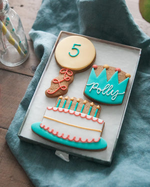 Honeywell Bakes Medium Birthday Party Biscuit Gift- Decorative cookies shaped like a balloon with a number 5 piped on, cake, and crown with personalised name on a blue cloth.