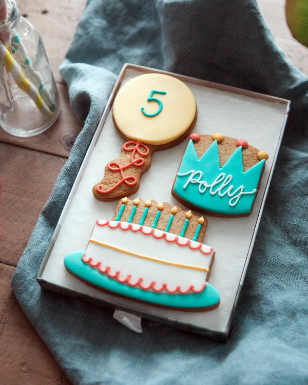 Honeywell Bakes Medium Birthday Party Biscuit Gift Decorative cookies shaped like a balloon with a number 5, a birthday cake, and crown with personalised name  on a blue cloth.
