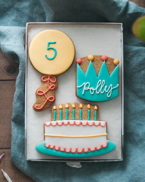 Honeywell Bakes Medium Birthday Party Biscuit Gift Decorative cookies shaped like a balloon with a number 5, a birthday cake, and crown with personalised name  on a blue cloth.