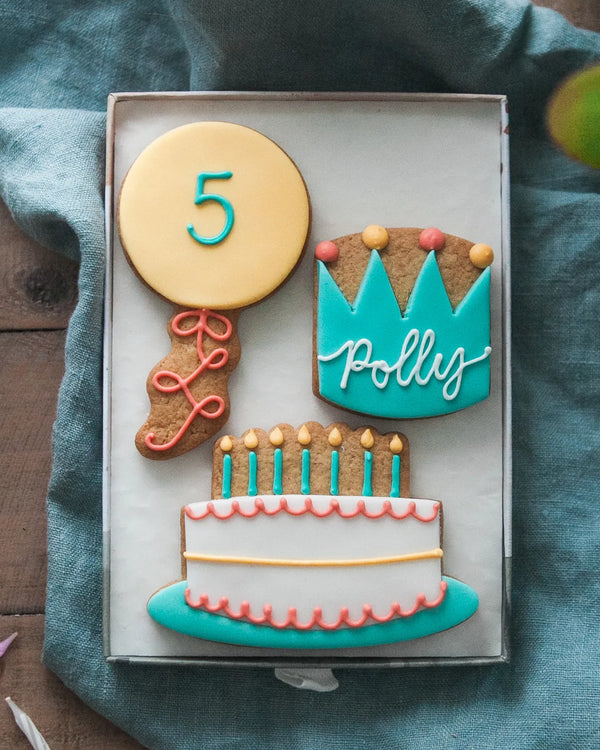 Honeywell Bakes Medium Birthday Party Biscuit Gift Decorative cookies shaped like a balloon with a number 5, a birthday cake, and crown with personalised name  on a blue cloth.