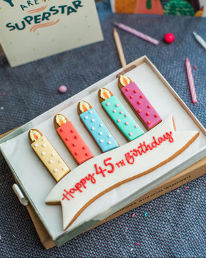 Honeywell Bakes Medium Personalised Birthday Candles Gift- Cookie set shaped like birthday candles with a decorative banner on a blue textured surface.