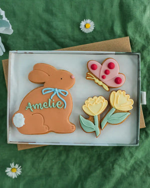 Honeywell Bakes Medium Personalised Meadow Bunny Biscuits - Decorative cookies shaped like a rabbit, butterfly, and flowers on a green fabric background.