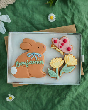 Honeywell Bakes Medium Personalised Meadow Bunny Biscuits - Decorative cookies shaped like a rabbit, butterfly, and flowers on a green fabric background.