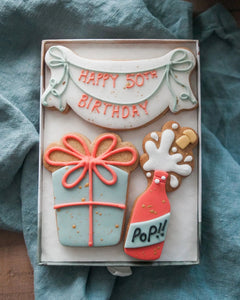 Honeywell Bakes Medium Happy Birthday Biscuit Gift - Cookies shaped like a birthday banner with Happy 50th Birthday, champagne bottle and present. Personalised.