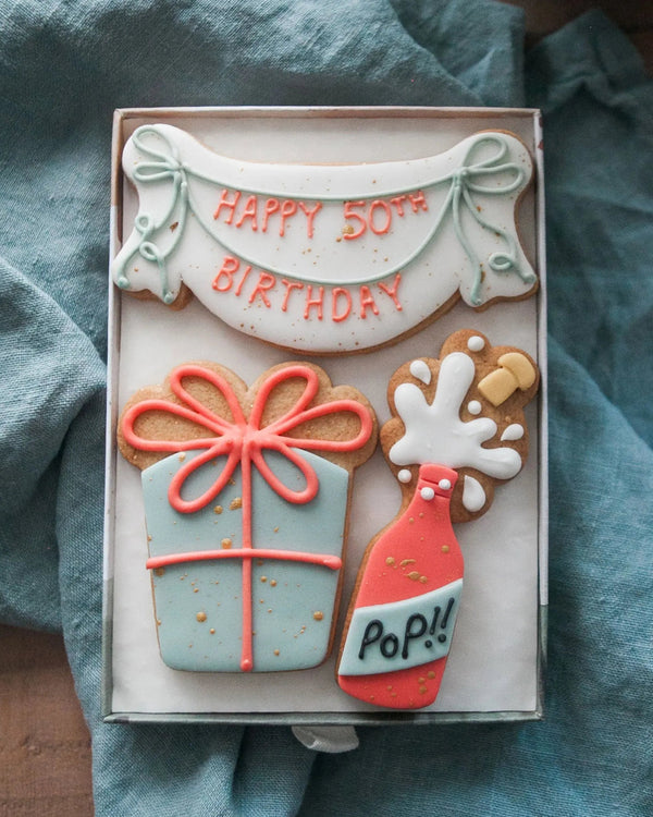 Honeywell Bakes Medium Happy Birthday Biscuit Gift - Cookies shaped like a birthday banner with Happy 50th Birthday, champagne bottle and present. Personalised.