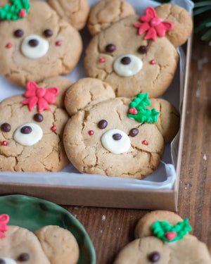 Honeywell Bakes - Decorated holiday teddy bear cookies arranged in a tray on a wooden table, with icing faces, chocolate eyes, and red and green icing accents.