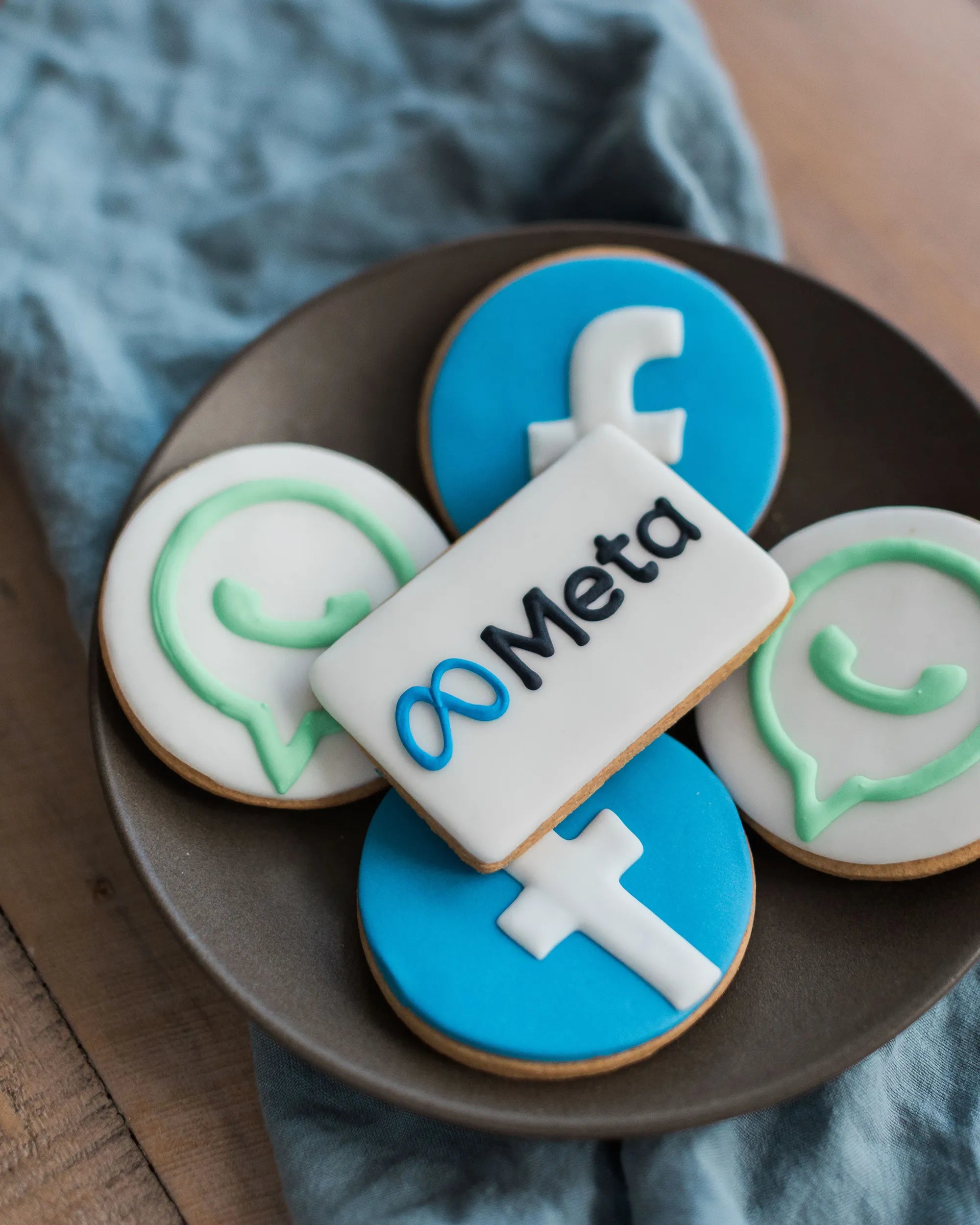 Honeywell Bakes branded biscuits; Four decorated cookies featuring blue and white Facebook-themed designs, a mint green WhatsApp-style logo on one white cookie, and a white rectangular cookie with the Meta logo