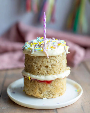 Honeywell Bakes Mini Celebration Cake Kit - Small layered birthday cake with a candle on a white plate, blurred background