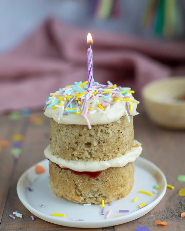 Honeywell Bakes Mini Celebration Cake Kit - Two-layered birthday cake with a lit candle on a wooden surface.