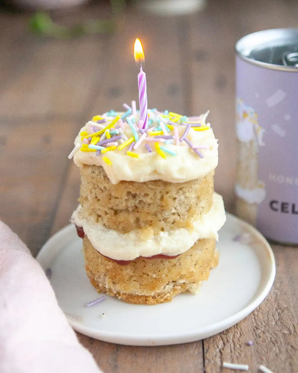 Honeywell Bakes Mini Celebration Cake Kit - Small birthday cake with a lit candle on a wooden table next to a can packaging.