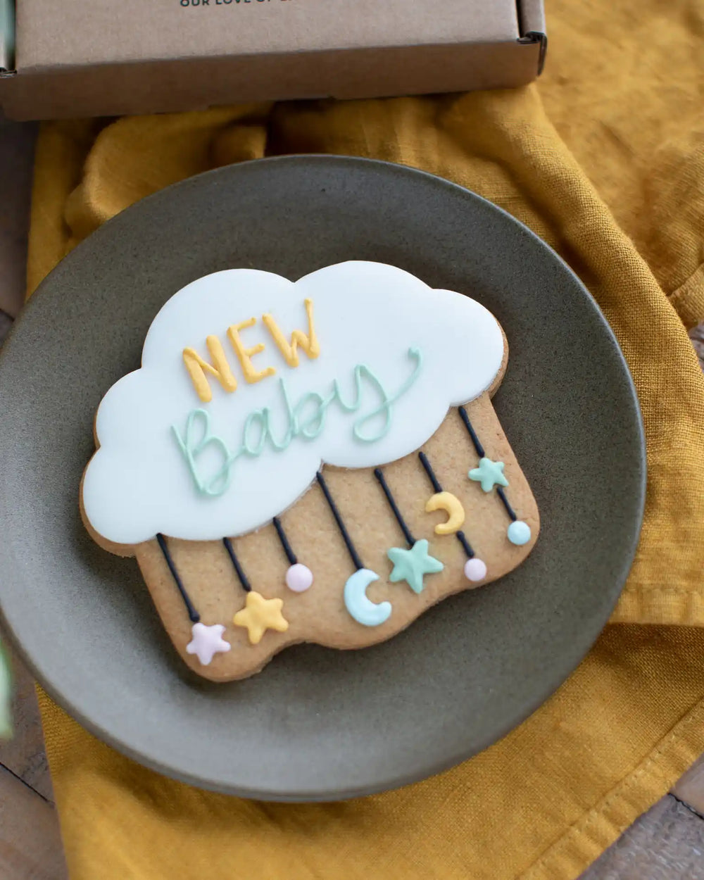 Honeywell Bakes New Baby Biscuit - Decorative cloud-shaped cookie with 'New Baby' text held by a person against a blue background