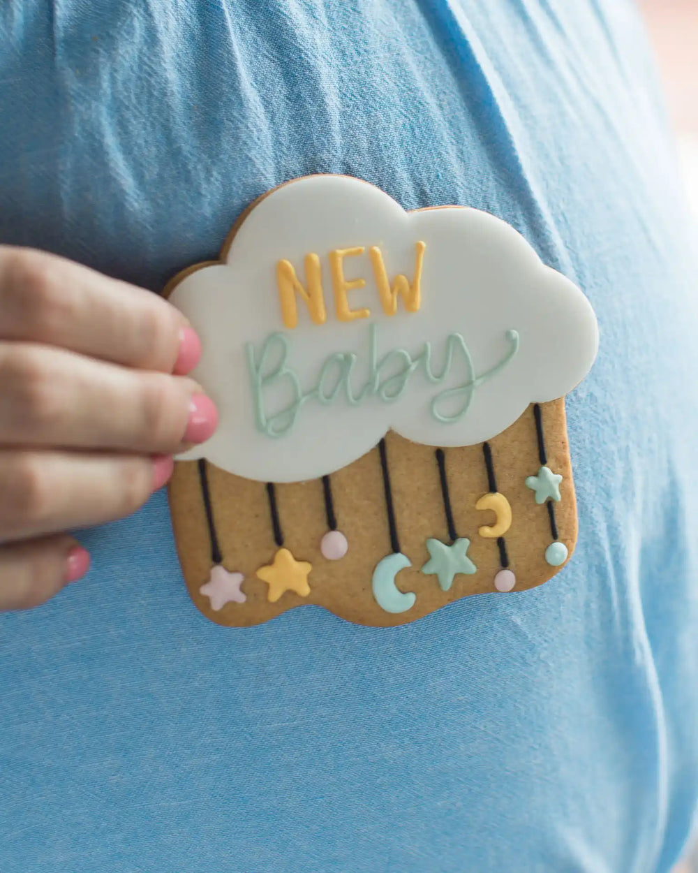 Honeywell Bakes New Baby Biscuit - Decorative cloud-shaped cookie with 'New Baby' text held by a person against a blue background