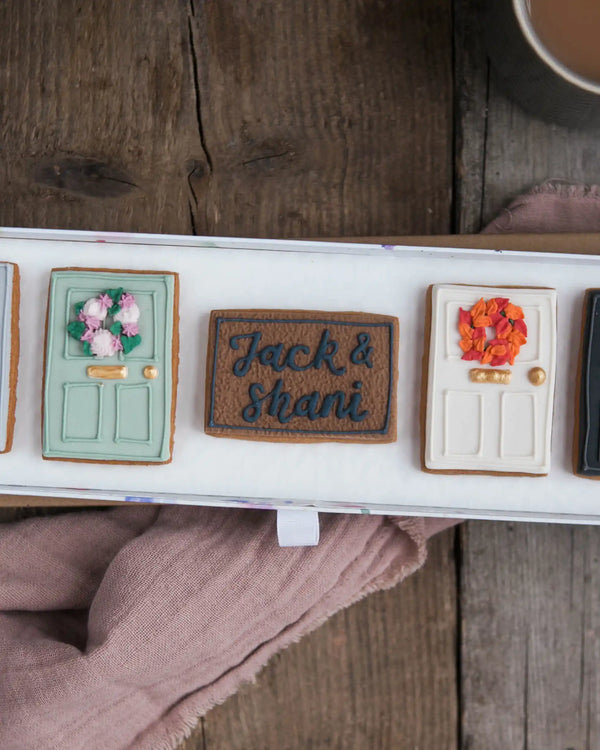 Honeywell Bakes New Home Biscuit Gift Set - Decorative cookies shaped like doors with personalized names on a wooden surface.