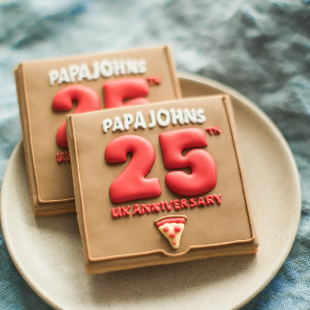 Two custom branded pizza box cookies celebrating Papa John's 25th UK anniversary on a plate.