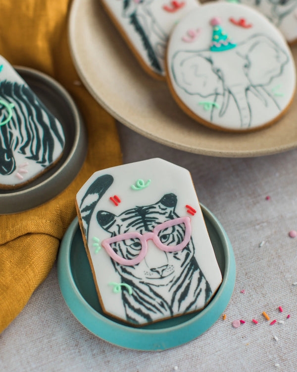 Honeywell Bakes Party Animal Biscuit Gift - Decorative cookies with zebra designs and pink glasses on a gray surface.