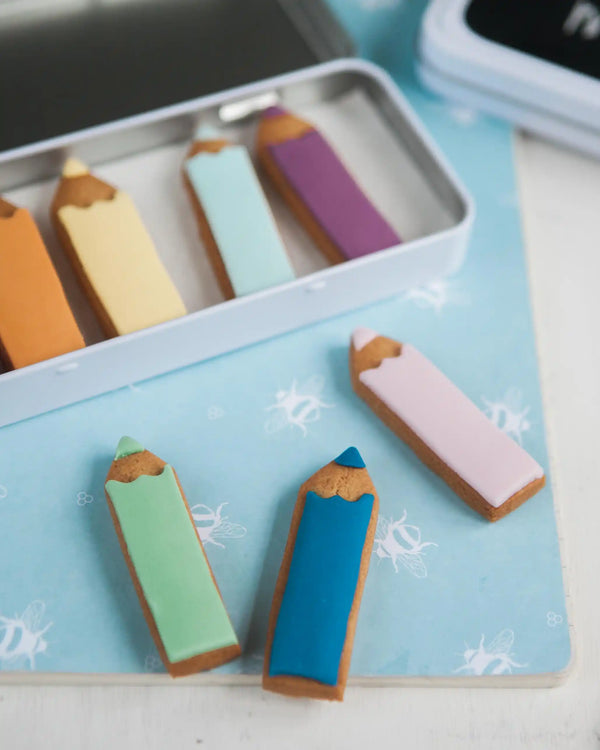 Honeywell Bakes Personalised Biscuit Pencils in Pencil Tin - Colourful pencil-shaped cookies on a blue tray with a white background