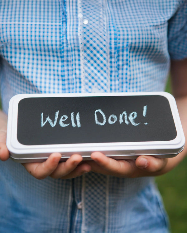 Honeywell Bakes Personalised Biscuit Pencils in Pencil Tin - Person holding a small chalkboard with 'Well Done!' written on it, wearing a blue checkered shirt.