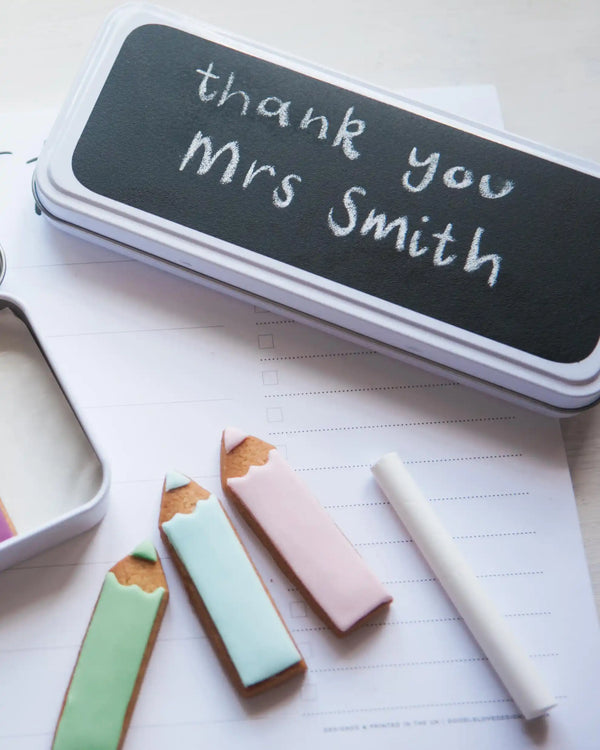 Honeywell Bakes Personalised Biscuit Pencils in Pencil Tin - Decorative cookies shaped like pencils and a chalk stick on a piece of paper with 'thank you Mrs Smith' written on it.