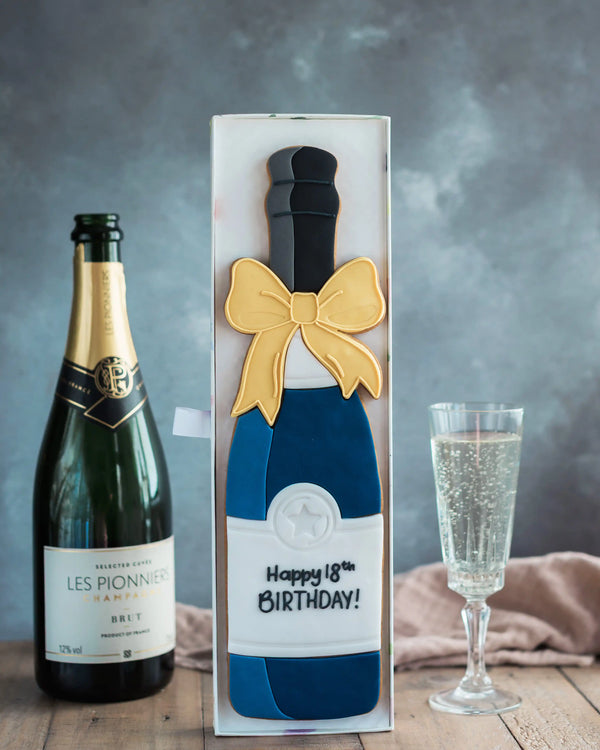 Honeywell Bakes Personalised Champagne Biscuit Bottle - Navy - A hand iced large biscuit in the shape of a champagne bottle next to a celebration glass