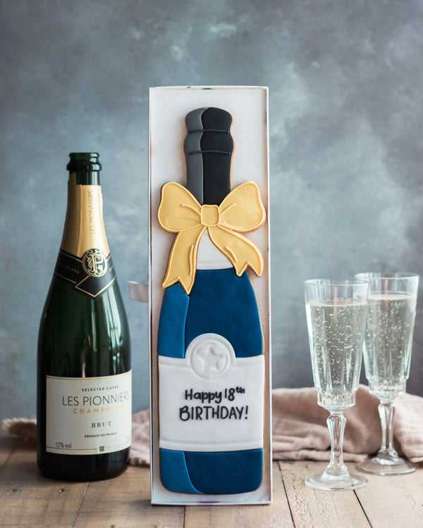 Honeywell Bakes Personalised Champagne Biscuit Bottle - Navy - A hand iced large biscuit in the shape of a champagne bottle next to a celebration glass