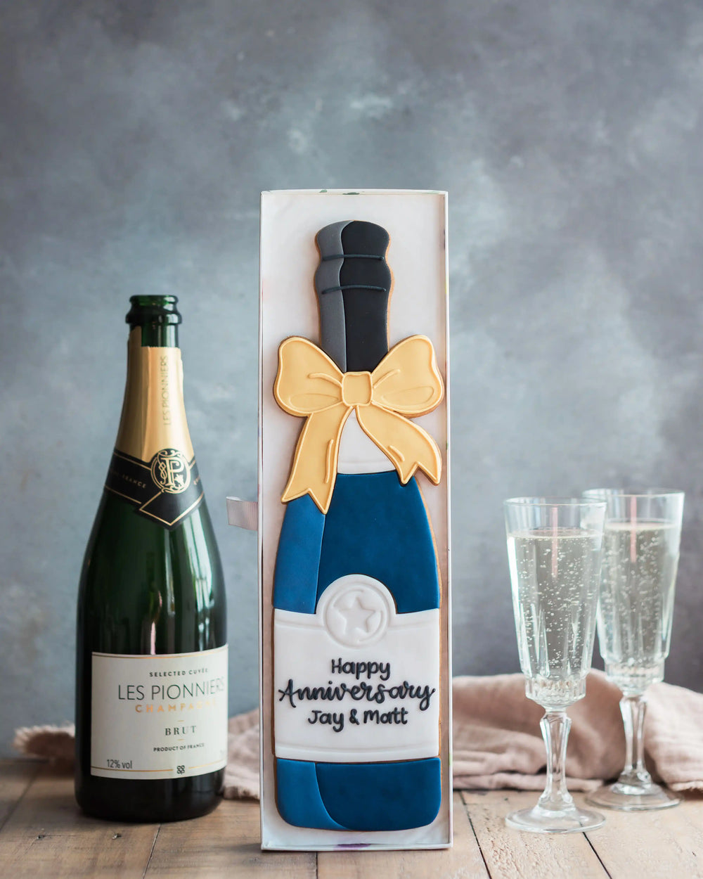 Honeywell Bakes Personalised Champagne Biscuit Bottle - Navy - A hand iced large biscuit in the shape of a champagne bottle next to a celebration glass