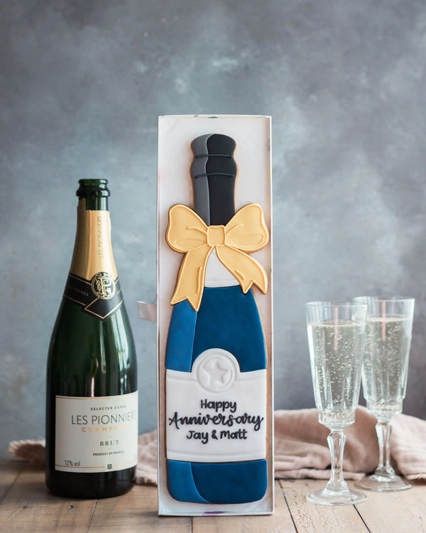 Honeywell Bakes Personalised Champagne Biscuit Bottle - Navy - A hand iced large biscuit in the shape of a champagne bottle next to a celebration glass
