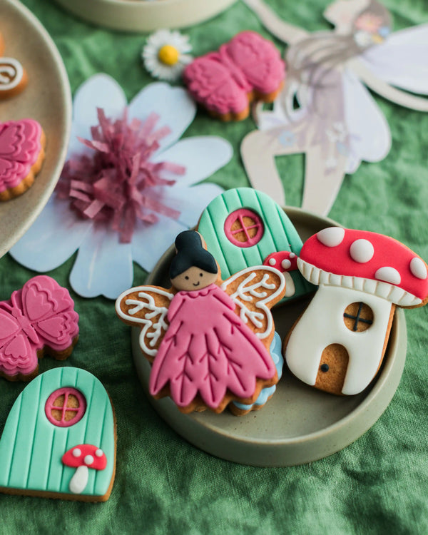 Honeywell Bakes Personalised Fairy Garden Biscuit Jar - Decorative cookies shaped like a fairy, mushroom, and fairy house on a green surface with flowers and a fairy figure.
