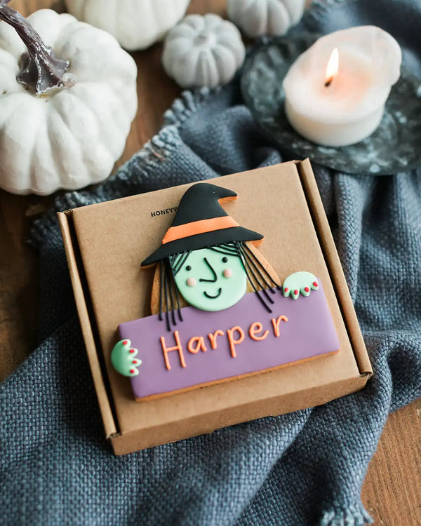 Honeywell Bakes Personalised Halloween Biscuit Witch - Halloween-themed cookie with a witch design in a box, surrounded by pumpkins and a candle.