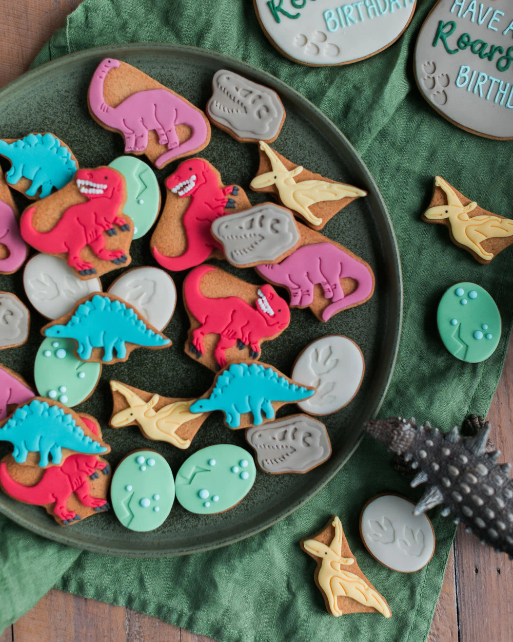 Honeywell Bakes Personalised Jar of Dinosaur Biscuits - Jar of dinosaur-shaped cookies with a 'Let's have a roarsome party!' label, surrounded by small dinosaur figurines.