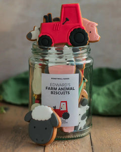 Honeywell Bakes Personalised Jar of Farm Animal Biscuits - Jar of cookies shaped like a red tractor, pig, and cow on a wooden surface.