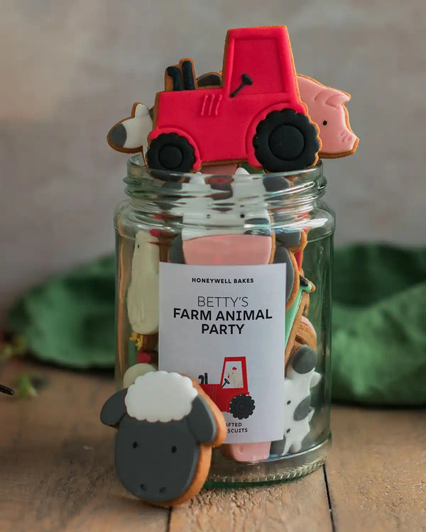 Honeywell Bakes Personalised Jar of Farm Animal Biscuits - Jar of farm-themed cookies with a red tractor, pink pig, and black sheep on top, featuring a 'Betty's Farm Animal Party' label.