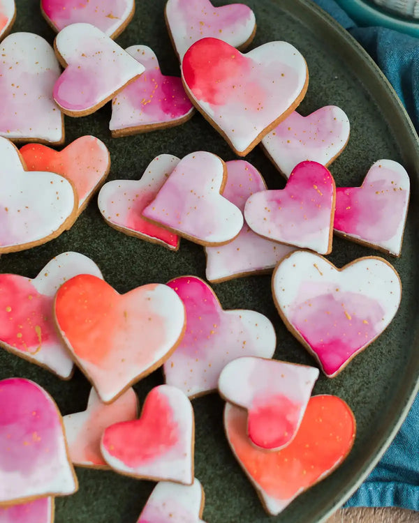 Honeywell Bakes Personalised Jar of Heart Biscuits - Heart-shaped cookies with pink and red gradient icing on a dark plate.