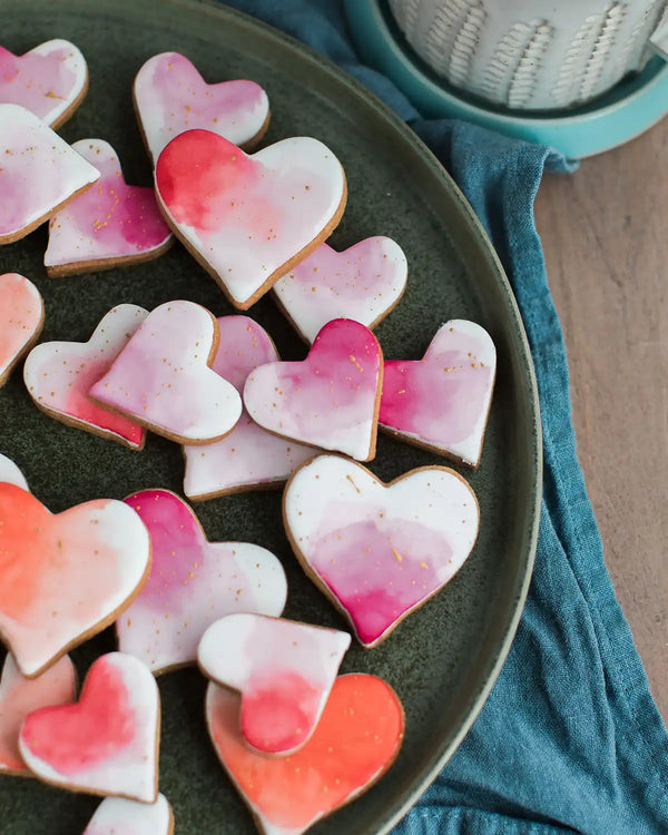 Honeywell Bakes Personalised Jar of Heart Biscuits - Heart-shaped cookies with pink and red watercolour design on a dark plate.