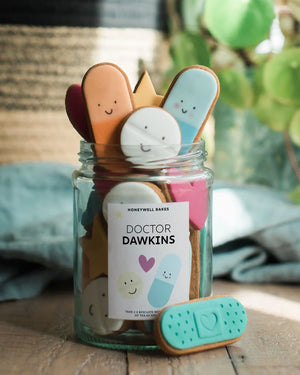Personalised jars of colourful biscuit pills decorated with smiley faces, hearts, plasters and stars, ideal for fun and thoughtful gifting.