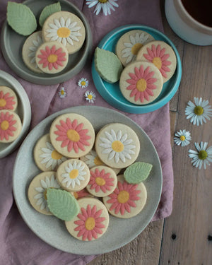Honeywell Bakes Personalised Jar of Shortbread Daisies - Decorative cookies shaped like flowers on a pink cloth with daisies.