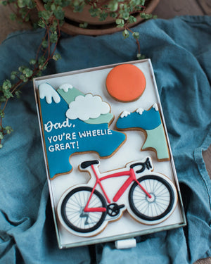 Honeywell Bakes Personalised Medium Bicycle Biscuit Gift - Biscuit box with bicycle design and 'Dad, you're wheelie great!' text on a blue fabric background.