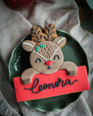 A Personalised Reindeer Biscuit, personalised with the name 'Leonora' in black royal icing, styled on a green plate.