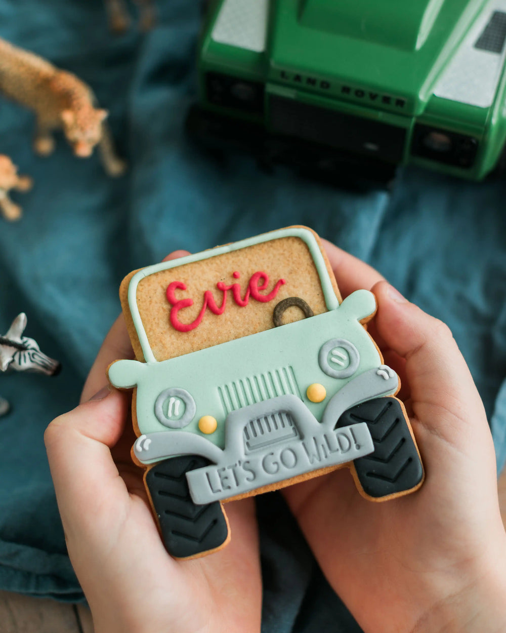 Honeywell Bakes Personalised Safari Car Biscuit - Cookie-shaped Jeep with 'Thank you' and 'Let's go wild!' text, held by hands with a blurred Land Rover in the background.