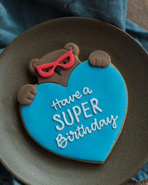 Honeywell Bakes Personalised Super Bear Hug Biscuit - A hand iced biscuit bear wearing a super hero mask and holding a love heart personalised with text Have a Super Birthday