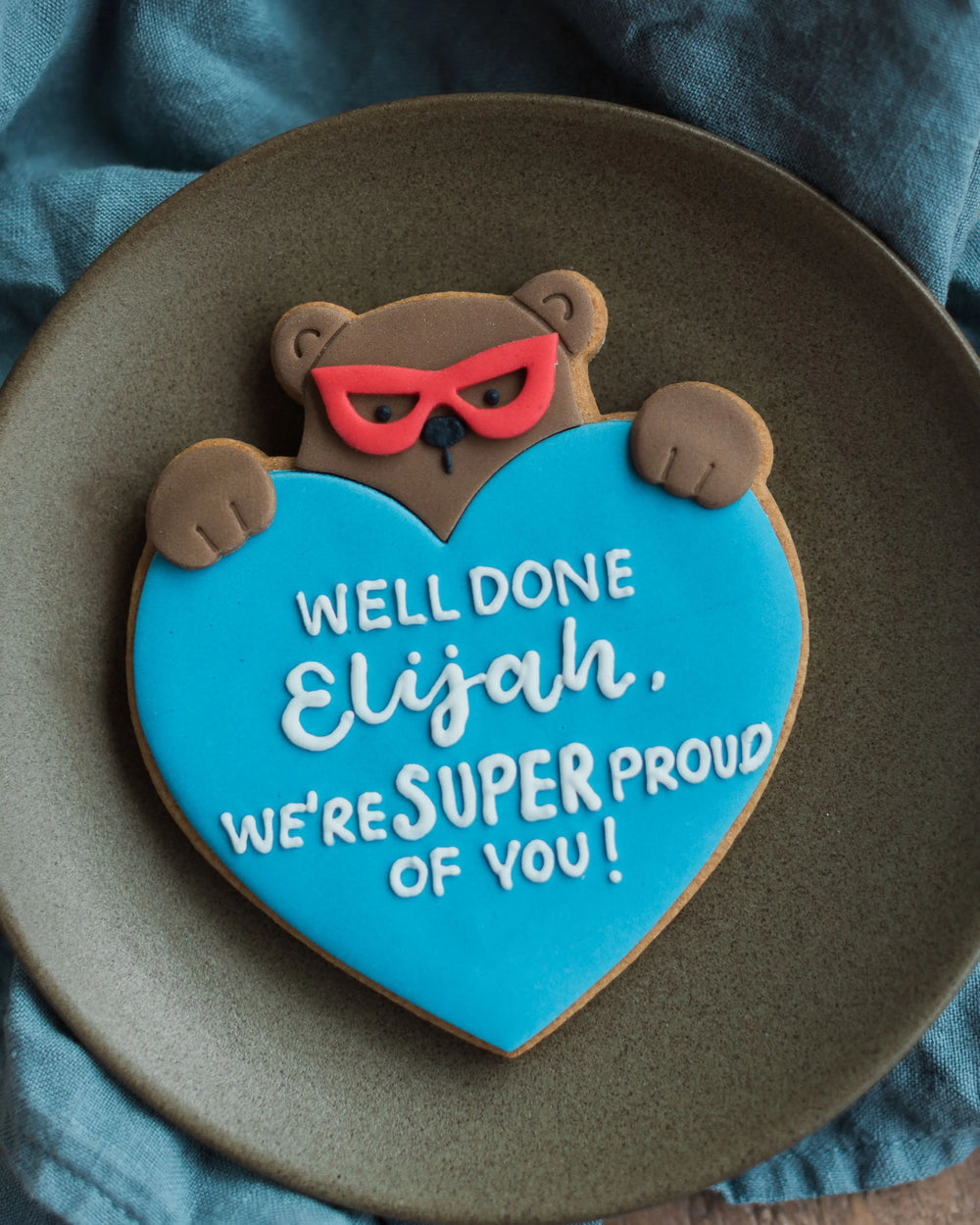 Honeywell Bakes Personalised Super Bear Hug Biscuit - A hand iced biscuit bear wearing a super hero mask and holding a love heart personalised with text Have a Super Birthday
