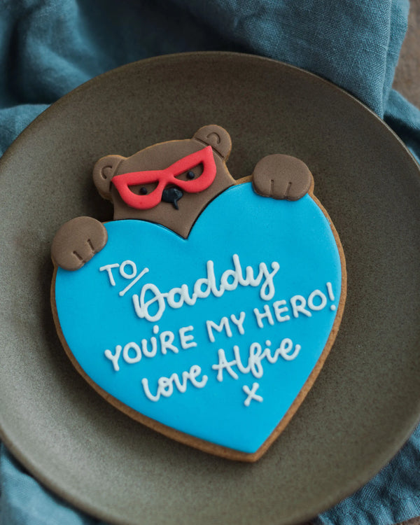 Honeywell Bakes Personalised Super Bear Hug Biscuit - A hand iced biscuit bear wearing a super hero mask and holding a love heart personalised with text To Daddy You’re My hero Love Alfie x