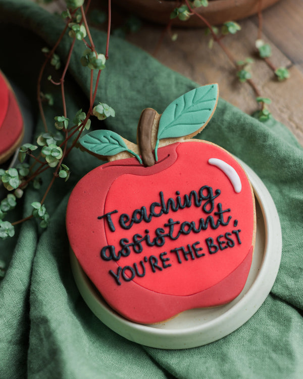 Honeywell Bakes Personalised Thank You Teacher Apple Biscuit - Cookie shaped like an apple with 'Teaching assistant, you're the best' text on a green background