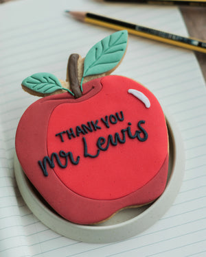 Honeywell Bakes Personalised Thank You Teacher Apple Biscuit - Cookie shaped like a red apple with 'Thank you Mr Lewis' text on a piece of paper.