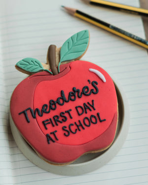 Honeywell Bakes Personalised Thank You Teacher Apple Biscuit - Cookie shaped like an apple with 'Theodore's First Day at School' text on a notebook page.