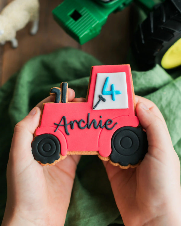 Honeywell Bakes Personalised Tractor Biscuit - Red toy tractor cookie with '4' and 'Archie' on a green fabric background