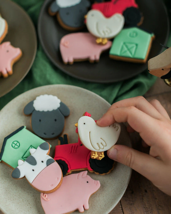 Honeywell Bakes Personalised Jar of Farm Animal Biscuits - Farm-themed cookies shaped like animals and a house on plates with a hand reaching for one of the cookies.